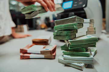 Image showing Bank employees using money counting machine while sorting and counting paper banknotes inside bank vault. Large amounts of money in the bank