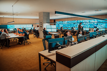 Image showing Group of Security data center operators working in a CCTV monitoring room looking on multiple monitors.Officers Monitoring Multiple Screens for Suspicious Activities