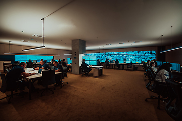 Image showing Group of Security data center operators working in a CCTV monitoring room looking on multiple monitors.Officers Monitoring Multiple Screens for Suspicious Activities