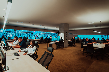 Image showing Group of Security data center operators working in a CCTV monitoring room looking on multiple monitors.Officers Monitoring Multiple Screens for Suspicious Activities