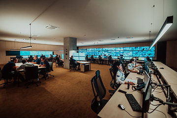 Image showing Group of Security data center operators working in a CCTV monitoring room looking on multiple monitors.Officers Monitoring Multiple Screens for Suspicious Activities