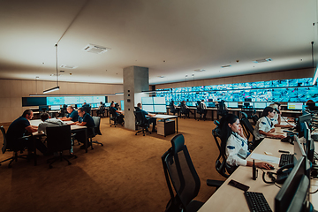 Image showing Group of Security data center operators working in a CCTV monitoring room looking on multiple monitors.Officers Monitoring Multiple Screens for Suspicious Activities