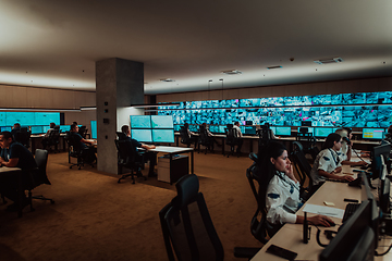 Image showing Group of Security data center operators working in a CCTV monitoring room looking on multiple monitors.Officers Monitoring Multiple Screens for Suspicious Activities