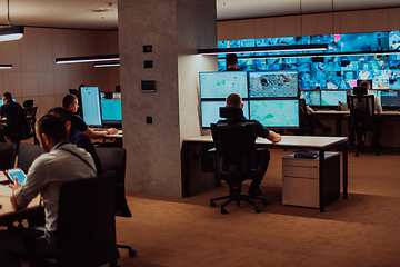 Image showing Group of Security data center operators working in a CCTV monitoring room looking on multiple monitors.Officers Monitoring Multiple Screens for Suspicious Activities