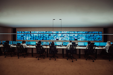 Image showing Group of Security data center operators working in a CCTV monitoring room looking on multiple monitors.Officers Monitoring Multiple Screens for Suspicious Activities