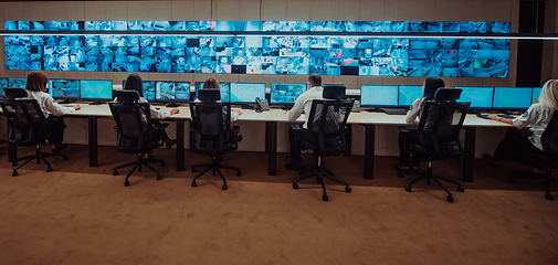 Image showing Group of Security data center operators working in a CCTV monitoring room looking on multiple monitors.Officers Monitoring Multiple Screens for Suspicious Activities