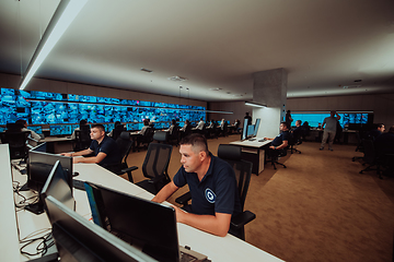 Image showing Group of Security data center operators working in a CCTV monitoring room looking on multiple monitors.Officers Monitoring Multiple Screens for Suspicious Activities