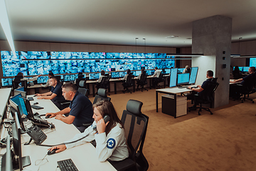 Image showing Group of Security data center operators working in a CCTV monitoring room looking on multiple monitors.Officers Monitoring Multiple Screens for Suspicious Activities