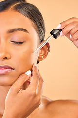 Image showing Face, skincare serum and woman with eyes closed in studio isolated on brown background. Dermatology, cosmetics and Indian female model apply hyaluronic acid, retinol or essential oil for healthy skin