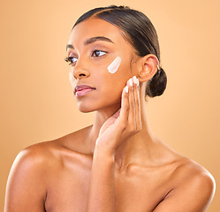 Image showing Face, beauty skincare and woman with cream in studio isolated on a brown background. Dermatology, cosmetics idea and thinking Indian female model with lotion, creme or moisturizer for skin health.