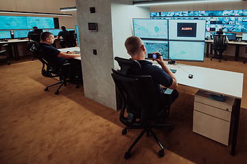 Image showing Group of Security data center operators working in a CCTV monitoring room looking on multiple monitors.Officers Monitoring Multiple Screens for Suspicious Activities