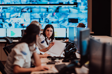 Image showing Group of Security data center operators working in a CCTV monitoring room looking on multiple monitors.Officers Monitoring Multiple Screens for Suspicious Activities