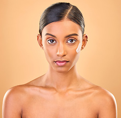 Image showing Face portrait, skincare and woman with cream in studio isolated on brown background. Dermatology, serious cosmetics and confident Indian female model with lotion, creme or moisturizer for skin health