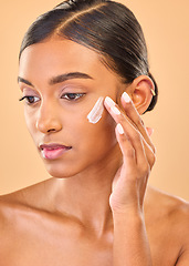 Image showing Face, beauty skincare and woman with cream in studio isolated on a brown background. Dermatology idea, cosmetics and thinking Indian female model apply lotion, creme and moisturizer for healthy skin.