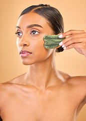 Image showing Face, beauty skincare and woman with gua sha in studio isolated on a brown background. Dermatology, thinking and serious Indian female model with jade crystal or stone for healthy skin treatment.