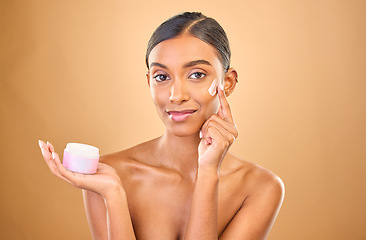 Image showing Face, skincare and woman with cream jar in studio isolated on a brown background. Dermatology cosmetics, portrait and happy Indian female apply lotion, creme and moisturizer product for healthy skin.