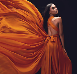 Image showing Fashion, woman and elegant, dress flying and style, beauty on dark background, portrait and model in orange in studio. Indian female, glamour and stylish with sexy person, luxury and designer wear