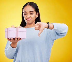 Image showing Gift, box and woman with thumbs down on yellow background for negative, disagreement and bad sign. Emoji mockup, sadness and girl holding present with dislike, unhappy and disappointed hand gesture