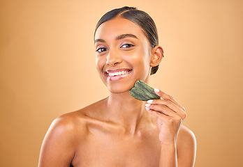 Image showing Face portrait, skincare and woman with gua sha in studio isolated on a brown background. Dermatology, facial massage or happy Indian female model with jade crystal or stone for healthy skin treatment