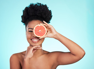 Image showing Black woman, face and smile with grapefruit for skincare nutrition, beauty or vitamin C against a blue studio background. Portrait of African female smiling with fruit for natural health and wellness