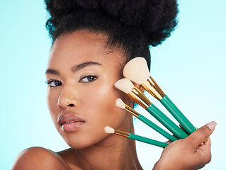Image showing Portrait, brushes and black woman with makeup, foundation and glow against a blue studio background. Face, Nigerian female and lady with cosmetic tools, grooming and morning routine for smooth skin