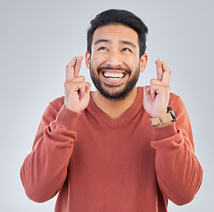 Image showing Thinking, luck and hand gesture with a man in studio on a gray background praying in hope of a miracle. Idea, smile and fingers crossed with a happy or handsome young male wishing for good fortune