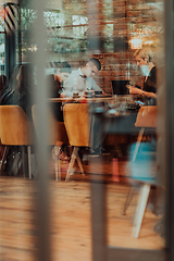 Image showing Photo through the glass of a group of business people sitting in a cafe and discussing business plans and ideas for new online commercial services