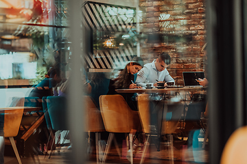 Image showing Photo through the glass of a group of business people sitting in a cafe and discussing business plans and ideas for new online commercial services