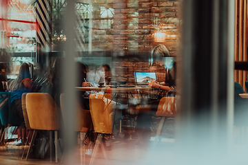 Image showing Photo through the glass of a group of business people sitting in a cafe and discussing business plans and ideas for new online commercial services