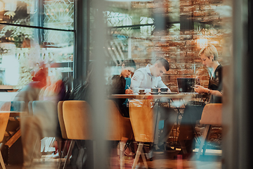 Image showing Photo through the glass of a group of business people sitting in a cafe and discussing business plans and ideas for new online commercial services