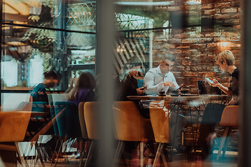 Image showing Photo through the glass of a group of business people sitting in a cafe and discussing business plans and ideas for new online commercial services