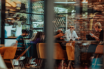 Image showing Photo through the glass of a group of business people sitting in a cafe and discussing business plans and ideas for new online commercial services