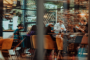 Image showing Photo through the glass of a group of business people sitting in a cafe and discussing business plans and ideas for new online commercial services