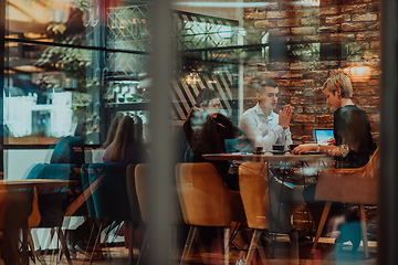 Image showing Photo through the glass of a group of business people sitting in a cafe and discussing business plans and ideas for new online commercial services