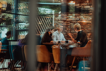 Image showing Photo through the glass of a group of business people sitting in a cafe and discussing business plans and ideas for new online commercial services