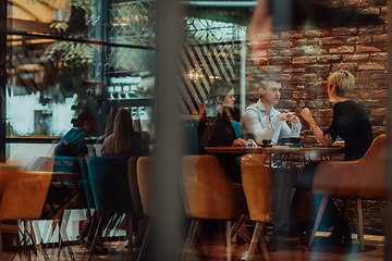 Image showing Photo through the glass of a group of business people sitting in a cafe and discussing business plans and ideas for new online commercial services