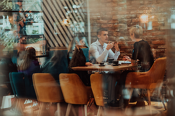 Image showing Photo through the glass of a group of business people sitting in a cafe and discussing business plans and ideas for new online commercial services