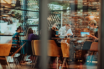 Image showing Photo through the glass of a group of business people sitting in a cafe and discussing business plans and ideas for new online commercial services