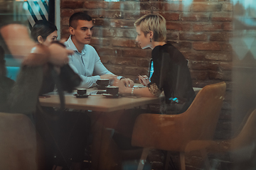 Image showing Photo through the glass of a group of business people sitting in a cafe and discussing business plans and ideas for new online commercial services