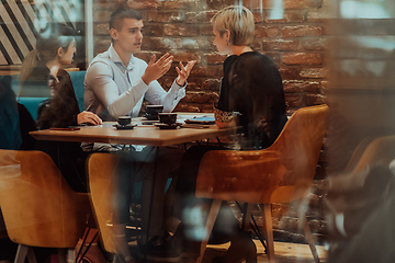 Image showing Photo through the glass of a group of business people sitting in a cafe and discussing business plans and ideas for new online commercial services