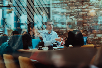 Image showing Photo through the glass of a group of business people sitting in a cafe and discussing business plans and ideas for new online commercial services