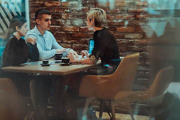 Image showing Photo through the glass of a group of business people sitting in a cafe and discussing business plans and ideas for new online commercial services