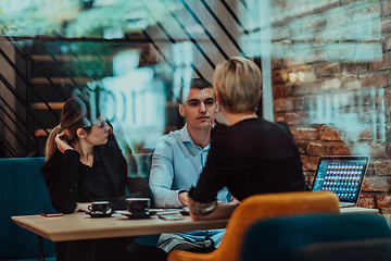 Image showing Photo through the glass of a group of business people sitting in a cafe and discussing business plans and ideas for new online commercial services