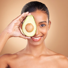 Image showing Indian woman, avocado and studio portrait for beauty, health and wellness with fruit by brown background. Asian young model and girl with organic self care with fruits, healthy cosmetic and skin glow
