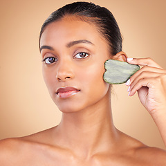 Image showing Beauty, gua sha and portrait of Indian woman for skincare, facial treatment and wellness with spa tools. Salon, dermatology and girl on brown background with cosmetics, face massage and luxury stone