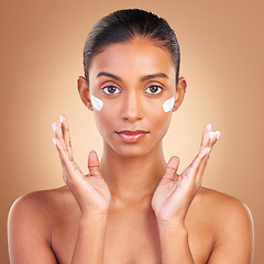 Image showing Indian woman, skincare cream and hands in portrait with health, serious or wellness by brown background. Young model, lotion product or face with aesthetic, dermatology and clean with cosmetic beauty