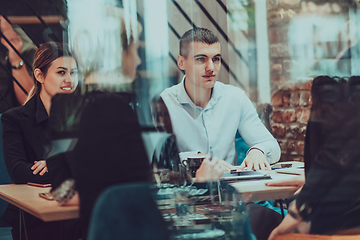 Image showing Photo through the glass of a group of business people sitting in a cafe and discussing business plans and ideas for new online commercial services