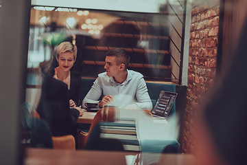 Image showing Photo through the glass of a group of business people sitting in a cafe and discussing business plans and ideas for new online commercial services