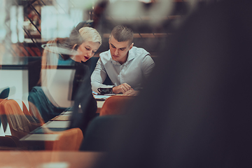 Image showing Photo through the glass of a group of business people sitting in a cafe and discussing business plans and ideas for new online commercial services