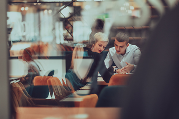 Image showing Photo through the glass of a group of business people sitting in a cafe and discussing business plans and ideas for new online commercial services